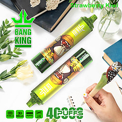 A Product Image Featuring Two Bang King Vape Devices With A Cartoon Gorilla Design, Labeled 'Strawberry Kiwi', Set Among Decorative Items Like Books And Flowers, With Product Features Like '40,000 Puffs' And 'Type-C' Specified Below.